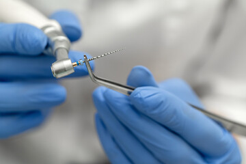Dental tools close-up. A drill for cleaning canals in the doctor’s hand with tweezers is mounted...