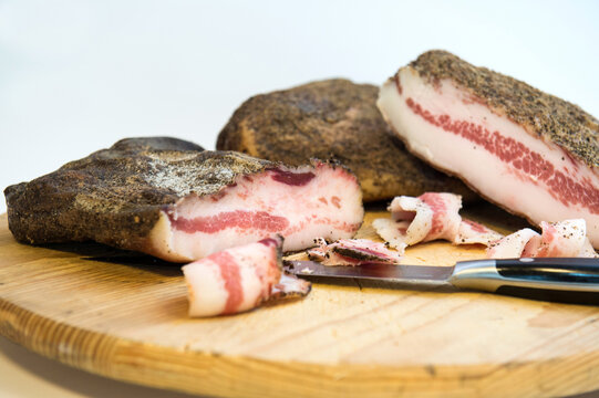 cut bacon. on the cutting board. bacon is called guanciale in Italy is made with the part of the throat of the pig seasoned with pepper and very fatty in a white background