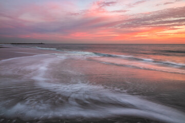 Waves retreating back into the sea under a soft vibrant pink and orange sky. 