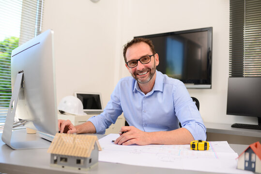 mature male architect working on laptop on new building project drawing sketch plan blueprint and making architectural construction house building in office studio workspace