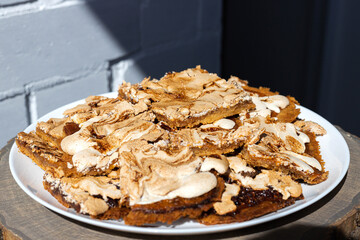 Oblong pieces of home-made crumble cake with strawberry jam covered with meringue on white plate served on wooden table. Streuselkuchen cake, idea for baking, close-up