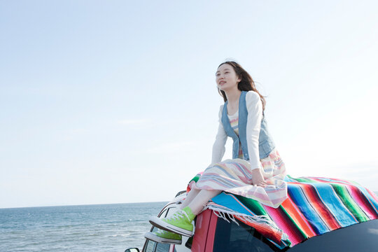 海沿いにとめた車の上に乗る10代の女の子