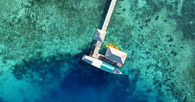 Aerial rotating view of a boat moored to a pontoon in the blue lagoon of Kanawa island with its coral reef, near the city of Labuan Bajo on Flores, Indonesia