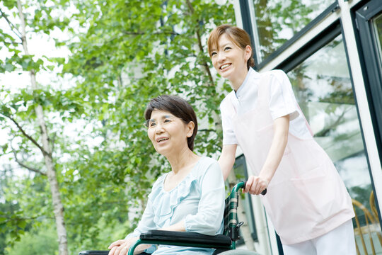 車いすを押す20代の女性介護士と60代の要介護者
