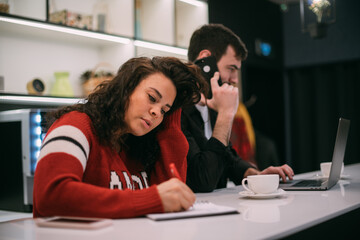 A man and a woman are working at a table in the kitchen.