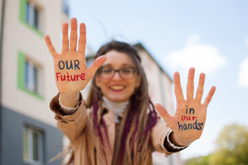 Modern girl with long dreadlocks and eyeglasses in nude color trench is showing hands with written...