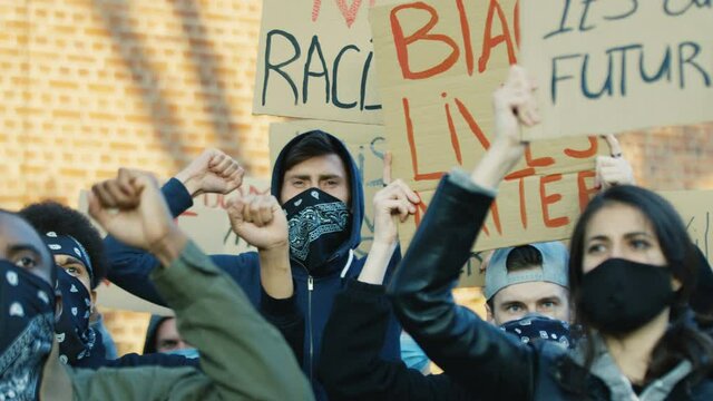 Multiethnic young male and female protesters in masks protesting against racism and police violence. Mixed-races people with posters shouting mottos at demonstration in USA. Activists for human rights