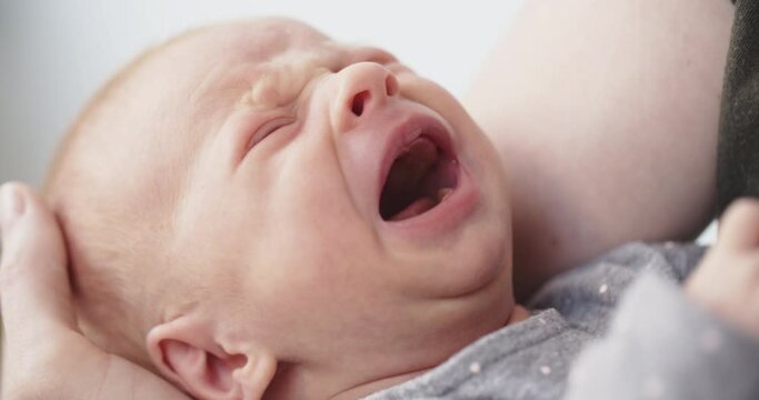 Closeup shot of a newborn baby girl crying in the arms of her mother.