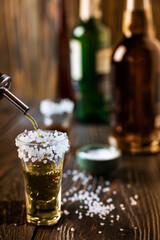 An alcoholic drink at the bar counter is poured into a tequila glass with salt at the edges, in the background are different bottles of alcohol, shallow depth of field, selective focus. The concept of