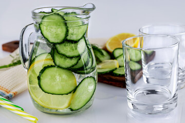 Cold drink made of cucumber and lemons, homemade lemonade in a decanter and two empty glasses, on a white background, shallow depth of field, selective focus. Healthy drinks concept