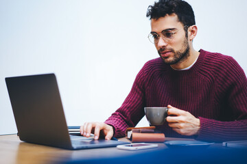 .Bearded freelancer in eyeglasses typing text information on digital laptop sitting in coworking