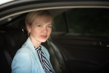 Fototapeta na wymiar happy young woman in a blue jacket in business clothes sitting in the back seat of a car with a laptop