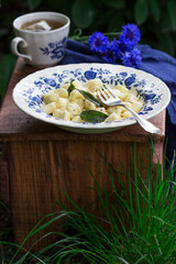 Breakfast of lazy dumplings with sage and chamomile tea on a wooden stool in the garden.