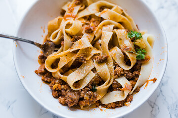 A delicious bowl of Italian beef bolognese meat sauce tossed with fresh pasta noodles and garnished with parsley. A fork is inside the noodles.