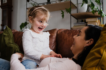 Young daughter and mother playing on the couch together, funny faces