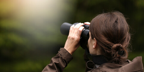 Young woman explorer with binoculars and telescope watching for animal in the wild forest.