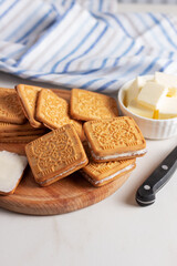 Butter spread on crispy square cookies on a wooden plate.