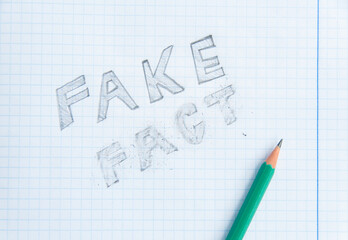 Fake news concept. Fake - Fact. Drawing in a notebook and pencil. Erased word fact. Fake information concept. Top view