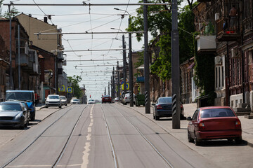 metal rails for a tram on a road on a city street with parked cars and old buildings. curve marking on the road. green public transport