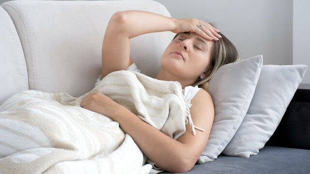 Sick young woman with headache lying on sofa at living room