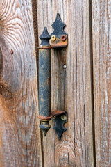 Old metal rusty handle painted in black and screwed to the wooden door with screws.