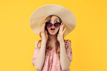 A shocked, thoughtful young attractive woman in a summer hat and sunglasses, on an yellow background