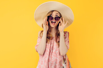 A shocked, thoughtful young attractive woman in a summer hat and sunglasses, on an yellow background