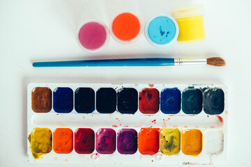 Colorful gouache paints and brush for painting on white wooden table. Copy, empty space for text