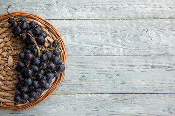 A cluster of dark grapes on a round straw tray and grey wooden table
