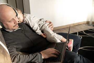 Father working at home with sleeping daughter  on his shoulder