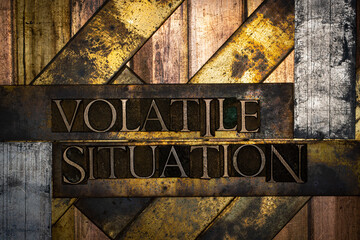 Photo of real authentic typeset letters forming text Volatile Situation on vintage textured silver grunge copper and gold background