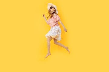 Fototapeta na wymiar happy girl in a summer hat and sunglasses in summer, jumping high on an yellow background