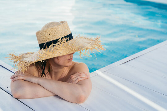 girl in a straw hat with arms crossed in a pool
