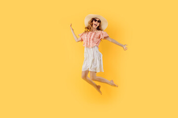 happy girl in a summer hat and sunglasses in summer, jumping high on an yellow background