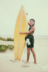 Young surfer girl poses with her surfboard on the beach