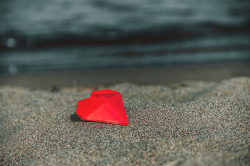 red origami paper heart lies in the sand