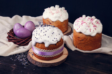 Easter cakes on a dark wooden background, decorated with lavender and marshmallows, and painted Easter eggs in a wicker nest.