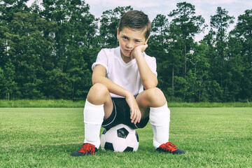 Little soccer player sitting on ball on the practice field