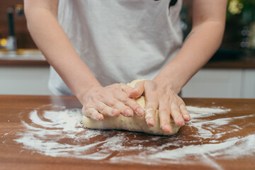 girl kneads dough on a wooden table in the kitchen
