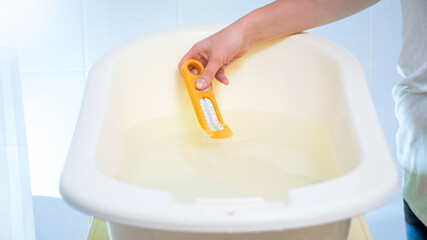 Young caring mother checking water temperature with termometer in bath for baby