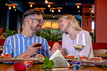 Happy young romantic couple in love drinking wine at dinner in a beautiful fancy restaurant.