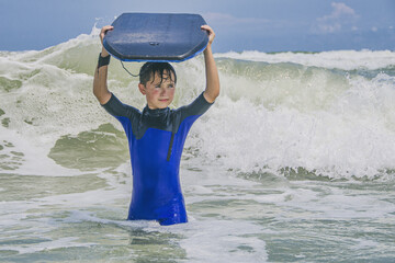 Boy in wet suit carrying boogie board in the surf