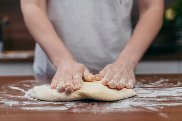 Fototapeta premium girl kneads dough on a wooden table in the kitchen 