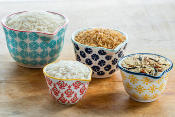 Assortment of dry rice in ceramic pots on wooden background
