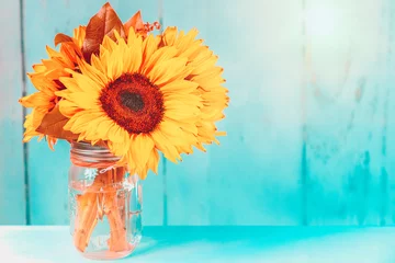 Zelfklevend Fotobehang Gloeiende zonnebloemen in een vaas met turkooizen achtergrond en kopieerruimte © Martina