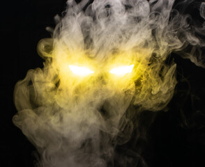 Ominous luminous eyes staring out of the darkness illuminate with a beam of yellow light swirling white smoke