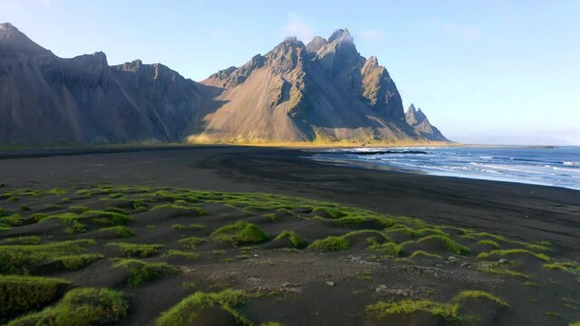 4k drone forward video (Ultra High Definition) of Stokksnes cape with Vestrahorn (Batman Mountain) on background. Panoramic Icelandic view of black sand dunes with fresh green grass. 