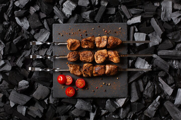 kebab on skewers. Three portions of grilled meat on a stone plate. Charcoal background. Top view.