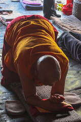 An old bold monk wearing traditional red and yellow cloathes praying in prostration in front of Jokhang temple in Lhasa on Barkhor square, Tibet
