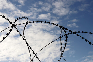 Silhouette of barbed wire on background of blue sky and white clouds. Concept of boundary, prison...